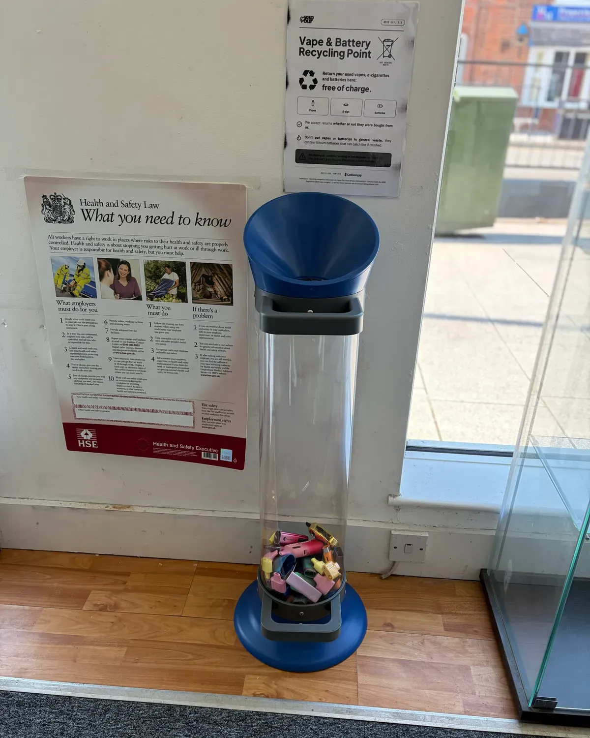 Vape recycling collection tube in use at an I Love Vapour store, with the takeback poster on the wall